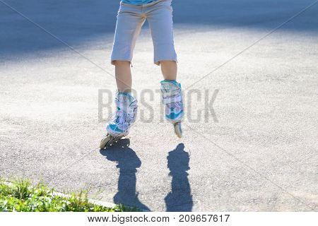 Legs of girl roller skating on playground at summer sunny day noface