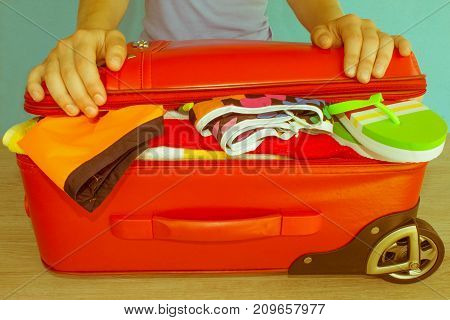 Young woman hands packing suitcase. Travel and vacations concept. Women's clothes and accessories in red suitcase things prepared for travel - Retro color