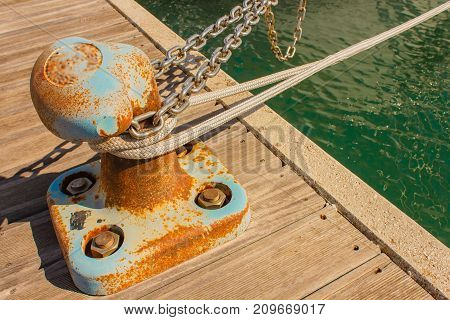 the bitt is a low cast-iron column in the shape of a mushroom to tie chains and mooring ropes /detail of a bitt with chains and ropes for mooring at the harbor