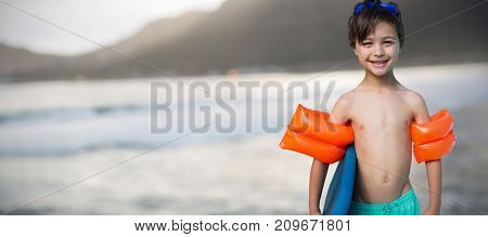 Portrait of shirtless boy carrying swimming float against mountain against sky at beach