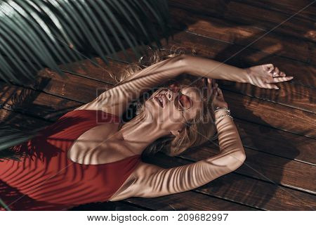 Total relaxation. Top view of beautiful young woman in swimwear keeping eyes closed and mouth open while lying under the palm tree