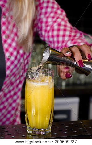The girl bartender makes a cocktail pours it into a glass standing on the bar. Female hands prepares a drink in the nightclub. Concept work in a club