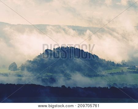 Distant Mountain Range And Heavy Clouds Of Colorful  Mist Above Deep Valleys