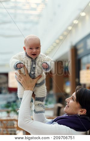 Young Caucasian Mom Is Playing With Her Cute Jolly Infant Son, Throwing Him Up And Catching Again At