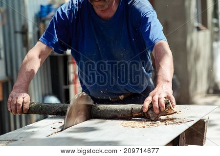 Man making firewood with buzz saw in the yard of private house.