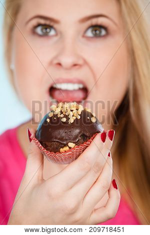 Diet sweets food concept. Woman holding delicious chocolate cupcake with peanut frosting having wide open mouth about to take bite