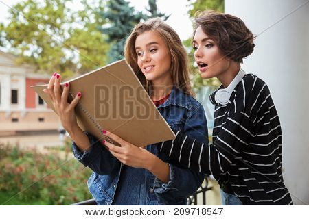 Two young pretty teenage girls studying together with a book outdoors