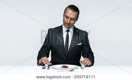 Portrait of a young man in image of maniak with knife, fork and and a piece of raw meat on a plate. Man in suit. The image in the style of Halloween