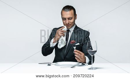 Portrait of a young man in image of maniak with knife, fork and and a piece of raw meat on a plate. Man in suit. The image in the style of Halloween