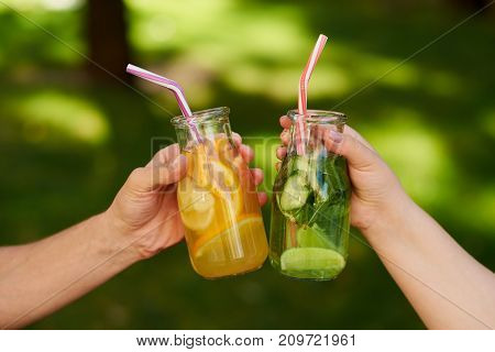 Friends celebrate with detox juice cocktailss on green nature background witn free space. Diet on the go, well being and weight loss, superfoods, health, vegetarian food concept