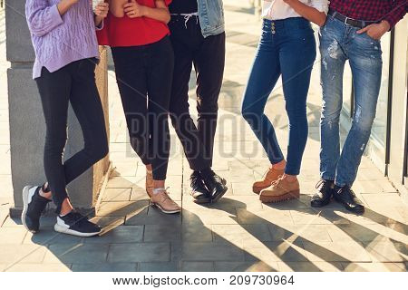 Legs of group of casual young people. Youth fashion. Crop of diverse informal students standing in row outdoors urban background