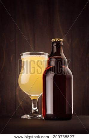 Brown beer bottle belgian steinie and glass tulip with muddy weizen on dark wood board vertical mock up. Template for advertising design branding identity.