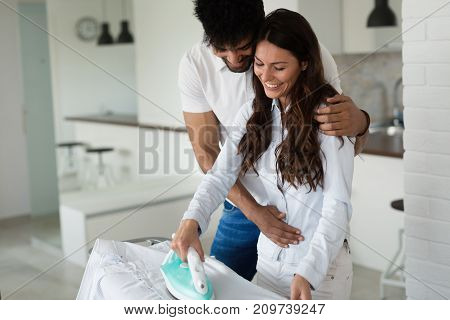 Young happy couple at home doing hosehold chores and ironing