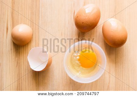 Fresh eggs in a cup and egg shell on wooden floor.