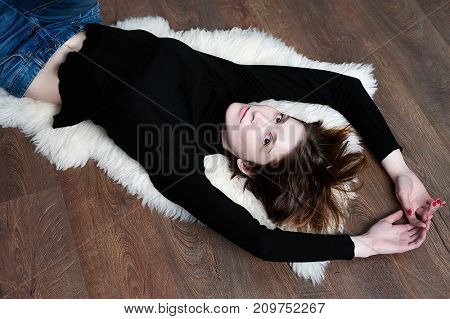 The portrait of a young woman with big sad eyes at studio. Closeup portrait of beautiful young woman lying on floor and looking at you