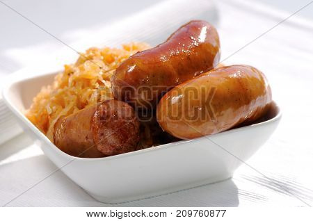 Grilled Sausages, Potatoes And Sauerkraut In A White Plate