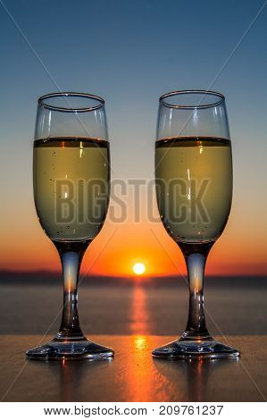 Couple of glasses of wine at sunset on the table, closeup, sun between glasses.
