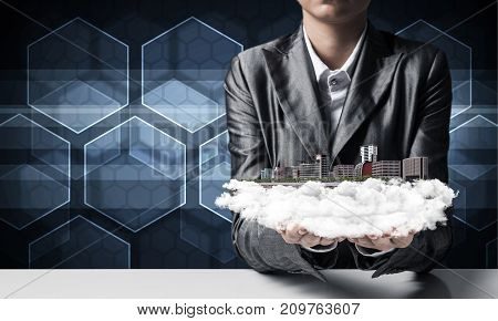 Cropped image of businessman in suit presenting in his hands modern city block with media icons on background. 3D rendering.