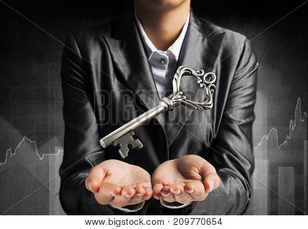 Cropped image of businessman in suit keeping big key in hands with business sketches on dark wall on background.