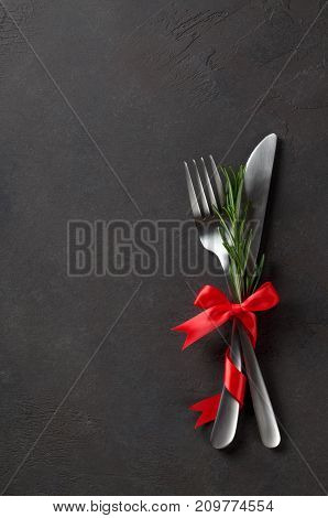 Festive set of knife and fork with red satin bow with rosemary dark stone slate background top view copyspace vertical image