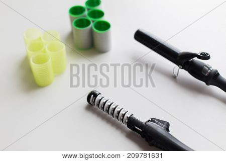 hair tools, beauty and hairdressing concept - curling irons or hot stylers and curlers on white background