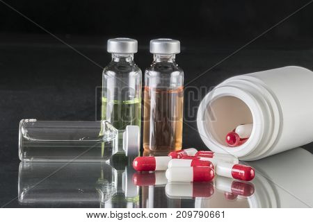 Some vials and boat of capsules red and white iinsolated on black background