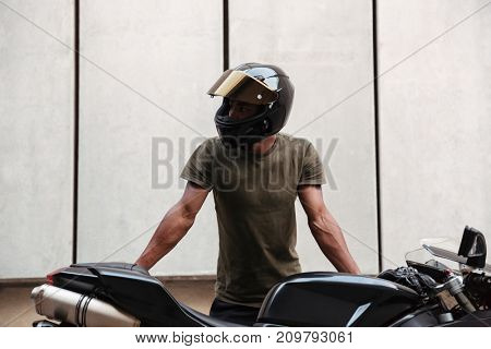 Portrait of a young afro american man in helmet leaning on a motorcycle and looking away outdoors