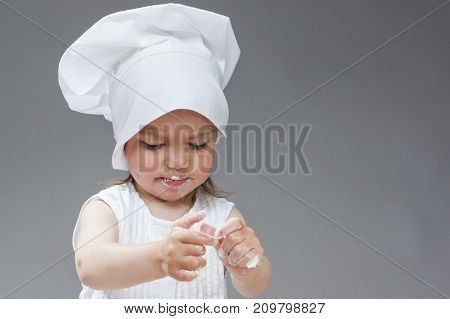 Portrait of Caucasian Little Girl in Cook Uniform Posing with Smudgy Face Against Gray Background. Horizontal Image Composition