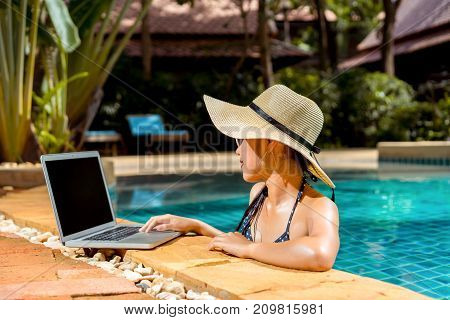 Woman bikini using laptop computer blank screen at swimming pool in resort edge relaxing hoildays