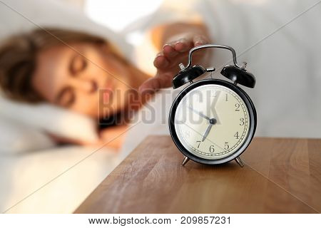 Sleepy young woman stretching hand to ringing alarm willing turn it off. Early wake up, not getting enough sleep, getting work concept