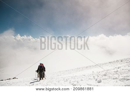 A group of mountaineers rises to the top of a snow-capped caucasian mountain against the backdrop of the rocky peaks of the mountains covered with snow.