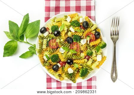 A photo of a plate of pasta salad with basil leaves, shot from above on a white background with a fork and a place for text