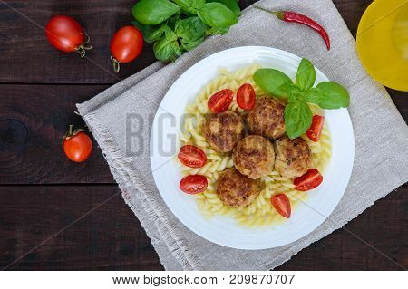 Pasta futsilli with meat balls cherry tomatoes basil on a white plate on a dark wooden background. Top view.