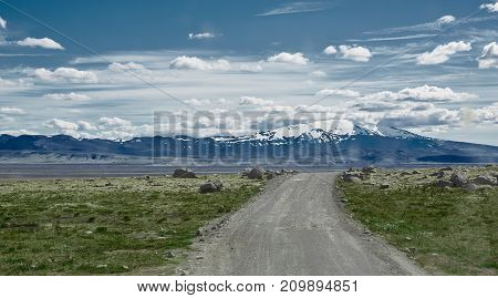 Travel to Iceland. road in a bright sunny mountain landscape. Vatna volcano covered with snow and ice on tne background.
