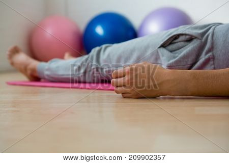 Low section of woman exercising while lying on mat in yoga studio
