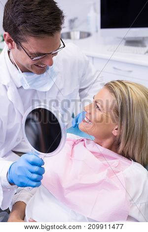 Doctor showing mirror to happy patient at dental clinic