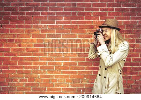 Happy young woman with retro photo camera over brick wall