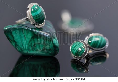 Closeup beauty silver earrings and ring with malachite on malachite stone piece on black acrylic desk.