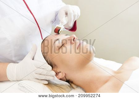 The woman undergoes the procedure of medical micro needle therapy with a modern medical instrument derma roller.