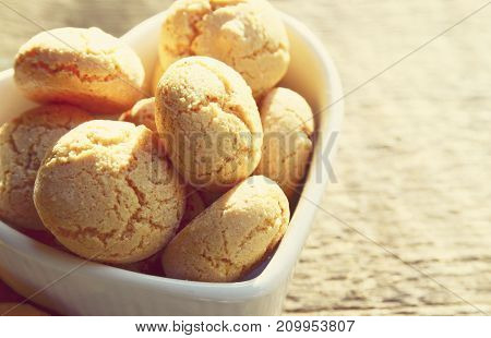 Italian Christmas cookies amaretti in a white heart shaped bowl.Tasty Italian amaretti biscuits on old wooden table.Amarettini cookies.Selective focus.