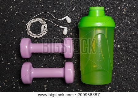 Small green dumbbells for fitness on a black background with a floor with a water bottle and headphones