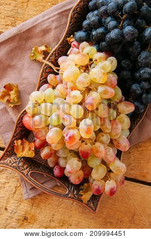 Bunches of fresh ripe grape served on a vintage tray on a wooden background. Close up and top view.