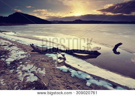 Broken Trunk Traped In Ice On Frozen Lake. Pond In Snowy Forest, Close Up. Frozen Bubbles Nad Cracks