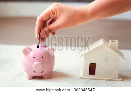 Woman Hand is Putting a Money Coin into Piggy Bank for Savings on The Bedroom., Female Hand is Inserting Coin in Pink Piggybank., Saving for Finance Future, Business Banking and Financial Real Estate