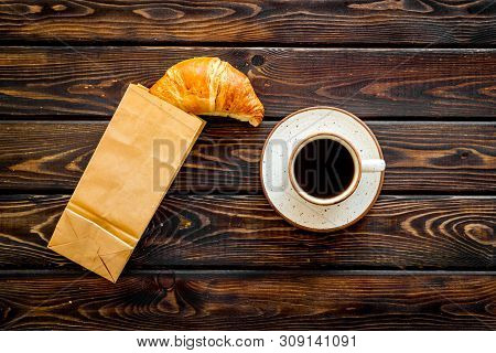 Breakfast With Croissant In Paper Bag And Cup Of Coffee On Wooden Background Top View