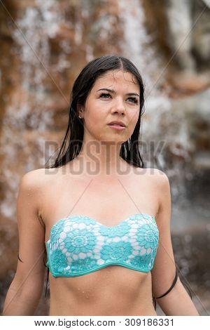 Wet Girl In A Bathing Suit Looks Into The Distance. In The Background Is A Rock And A Waterfall