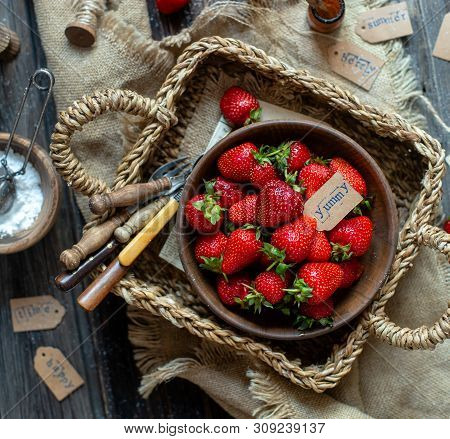 Overhead Shot Of Tasty Ripe Strawberries In Wooden Bowl Stands In Wicker Strawy Basket On Rustic Tab
