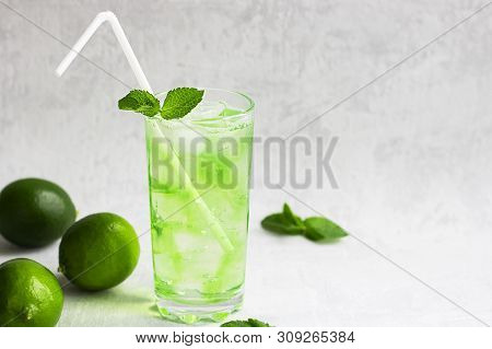 Summer Cold Green Drink With Lime, Mint And Lemon In Tall Glass With Ice And Straw And Defocused Fru