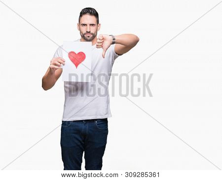 Handsome young man holding card with red heart over isolated background with angry face, negative sign showing dislike with thumbs down, rejection concept