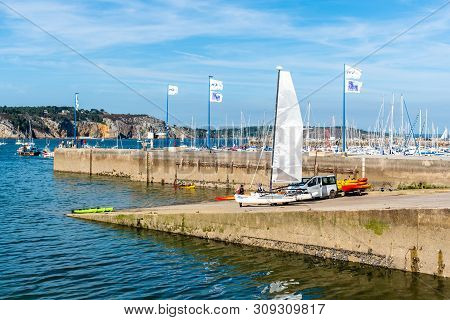 Morgat, France - August 4, 2018:  People taking out the water and storing canoes, kayaks and a catamaran in the marina of Morgat a sunny day of summer